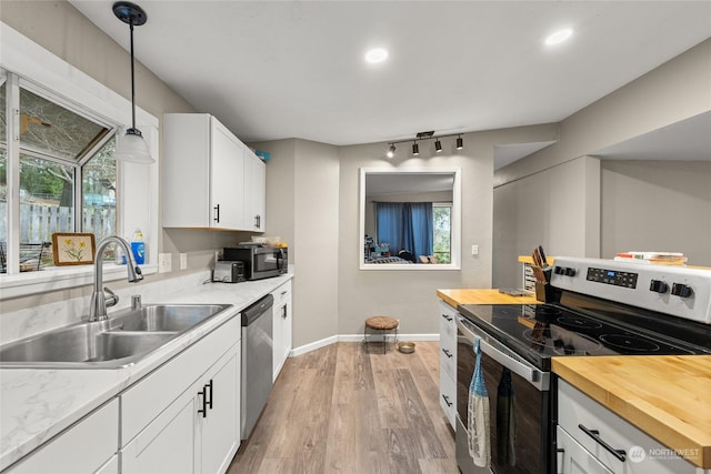 kitchen with appliances with stainless steel finishes, sink, butcher block countertops, white cabinetry, and hanging light fixtures