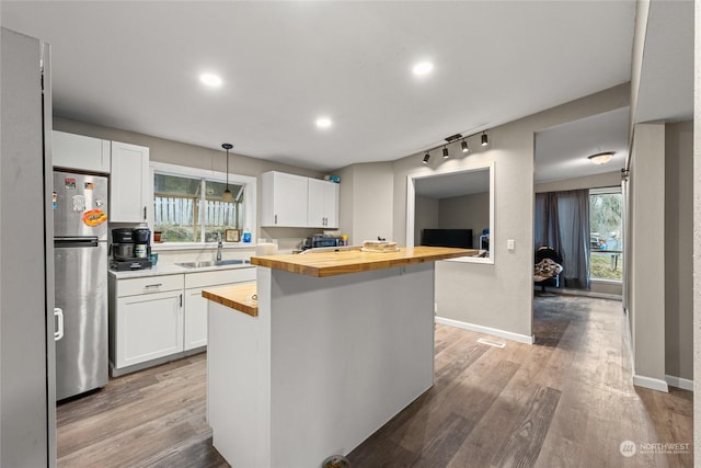 kitchen with butcher block counters, stainless steel fridge, white cabinets, and decorative light fixtures