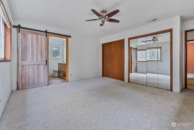 unfurnished bedroom with carpet, a barn door, ensuite bathroom, and ceiling fan