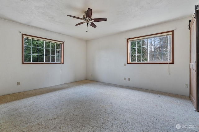 unfurnished room with carpet flooring, a barn door, and ceiling fan