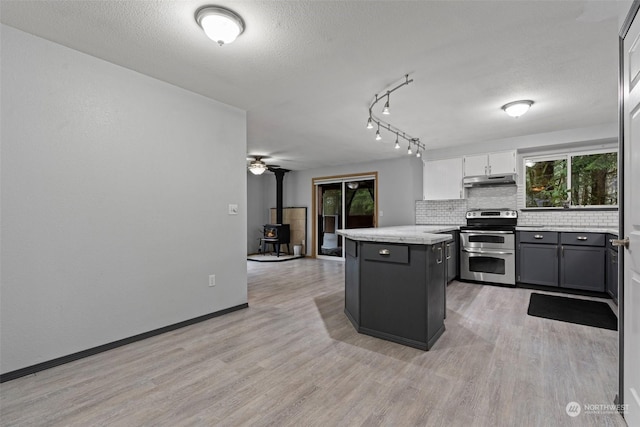 kitchen featuring a wood stove, a center island, stainless steel range with electric cooktop, light hardwood / wood-style floors, and white cabinets