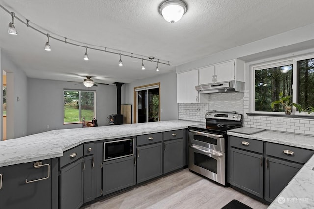 kitchen with ceiling fan, stainless steel electric stove, built in microwave, gray cabinets, and a wood stove