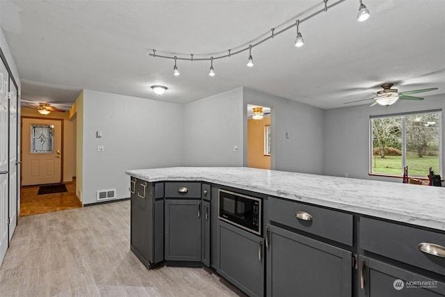 kitchen with light stone counters, ceiling fan, built in microwave, gray cabinets, and light hardwood / wood-style floors