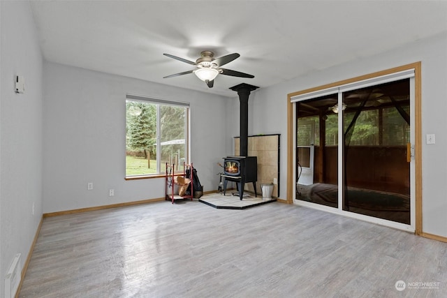 unfurnished living room featuring ceiling fan, a wood stove, and light hardwood / wood-style flooring