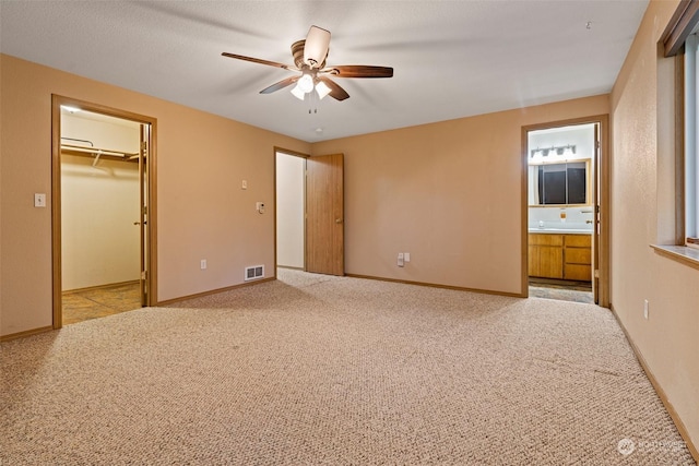 unfurnished bedroom featuring a walk in closet, ensuite bath, light colored carpet, ceiling fan, and a closet