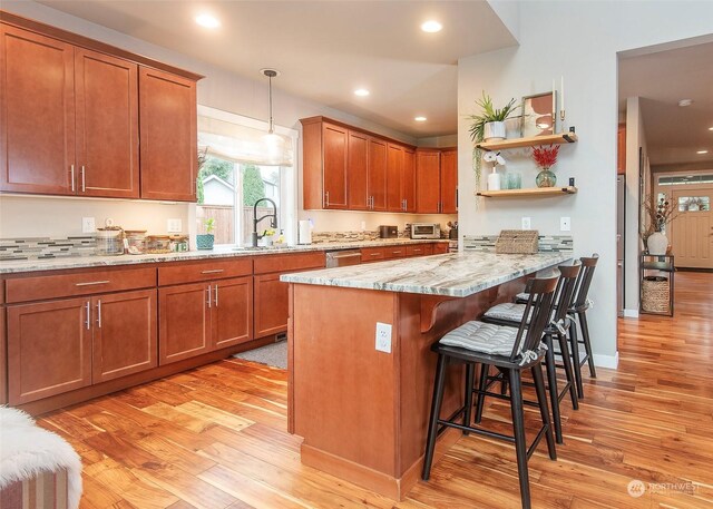 kitchen featuring sink, hanging light fixtures, light wood-type flooring, light stone countertops, and a kitchen bar