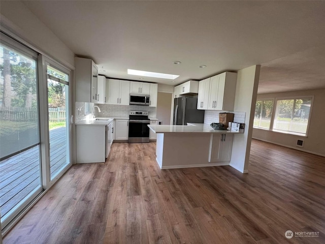 kitchen with sink, kitchen peninsula, white cabinets, stainless steel appliances, and backsplash