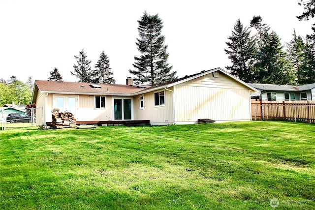 rear view of property with a chimney, french doors, a fenced backyard, and a yard