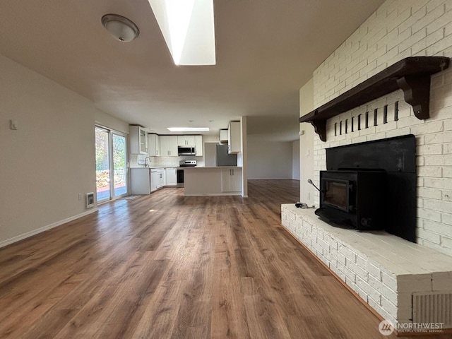 unfurnished living room featuring a sink, a fireplace, visible vents, baseboards, and wood finished floors