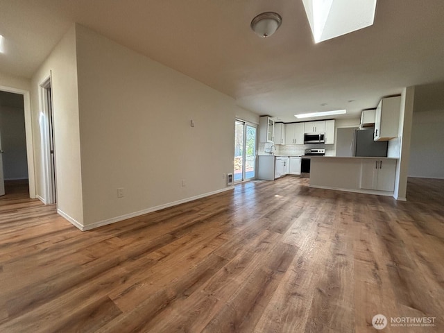 unfurnished living room featuring baseboards, wood finished floors, and a skylight