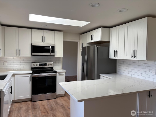 kitchen featuring light stone countertops, stainless steel appliances, light wood-type flooring, a skylight, and white cabinets