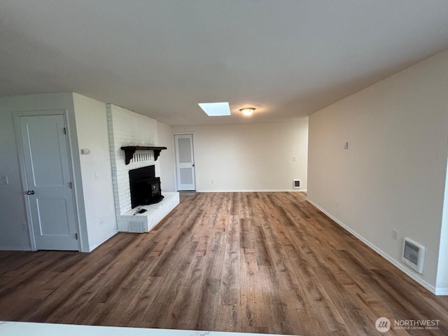 unfurnished living room featuring a brick fireplace, visible vents, baseboards, a skylight, and wood finished floors