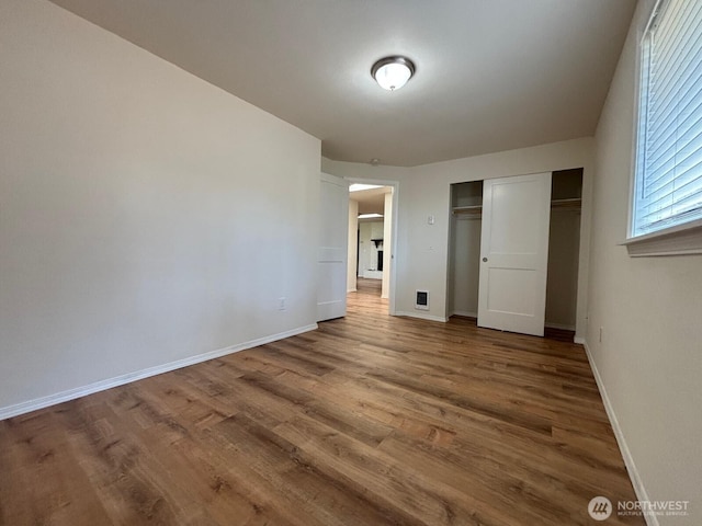 unfurnished bedroom featuring wood finished floors, a closet, visible vents, and baseboards