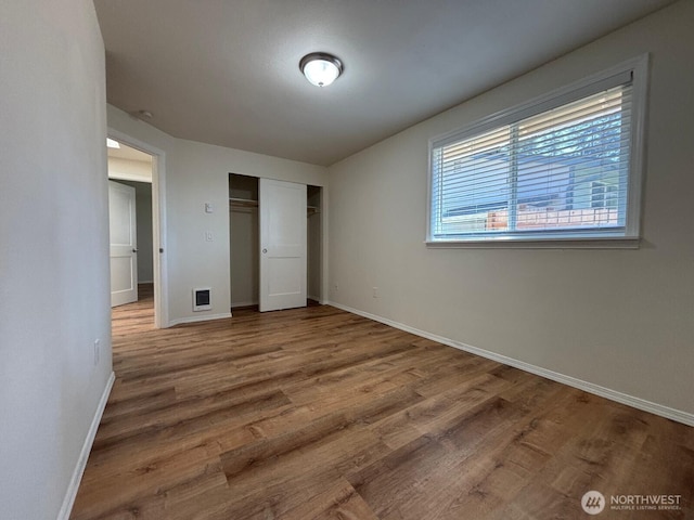 unfurnished bedroom featuring wood finished floors, a closet, visible vents, and baseboards