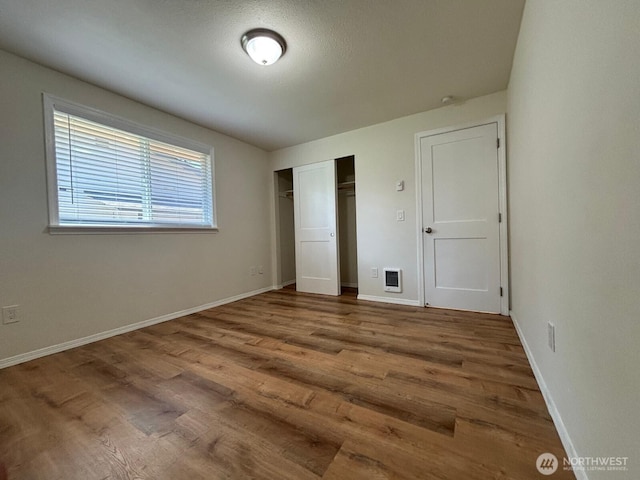 unfurnished bedroom featuring wood finished floors, a closet, visible vents, and baseboards