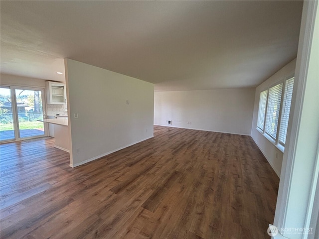 unfurnished living room featuring dark wood-style floors, baseboards, and a healthy amount of sunlight
