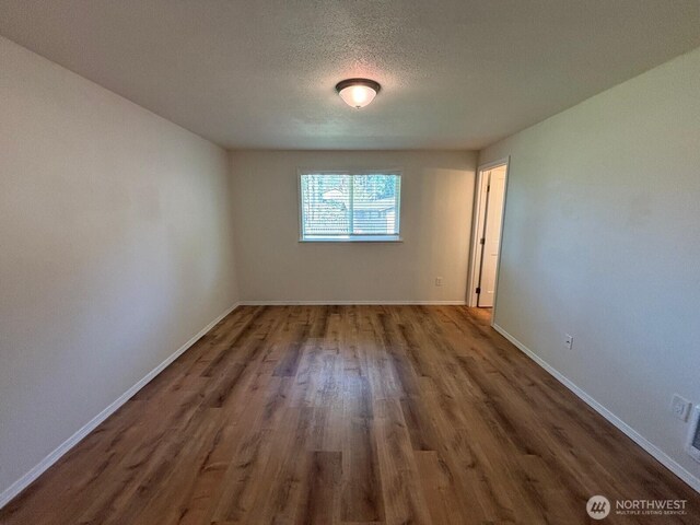 unfurnished room with baseboards, wood finished floors, and a textured ceiling