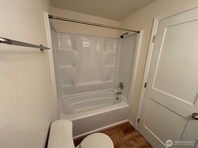 bathroom featuring wood finished floors, toilet, washtub / shower combination, and a textured wall