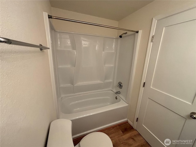 full bath with shower / washtub combination, wood finished floors, toilet, and a textured wall