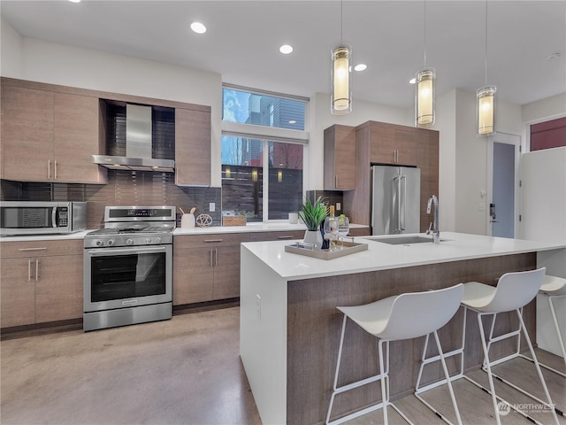 kitchen with pendant lighting, stainless steel appliances, a kitchen island with sink, and wall chimney exhaust hood