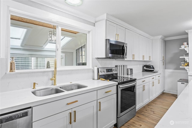 kitchen with a skylight, sink, white cabinets, and appliances with stainless steel finishes