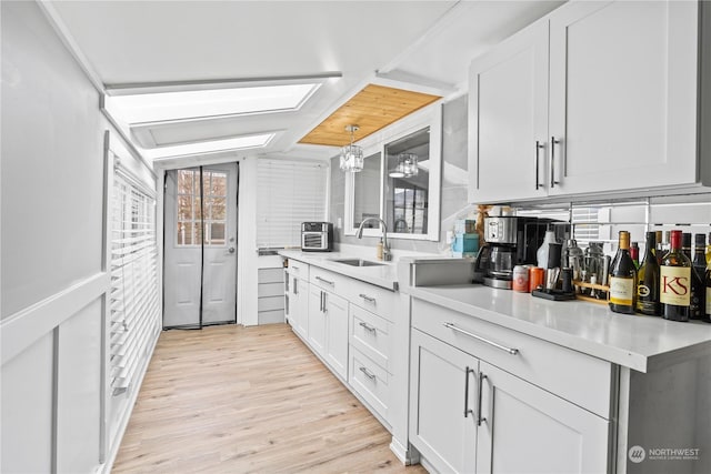 kitchen with light hardwood / wood-style floors, white cabinetry, hanging light fixtures, and sink