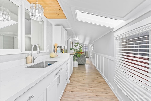 bar with sink, hanging light fixtures, light stone counters, light hardwood / wood-style floors, and white cabinets