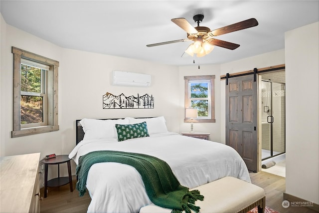 bedroom with light hardwood / wood-style flooring, ceiling fan, a barn door, connected bathroom, and a wall unit AC