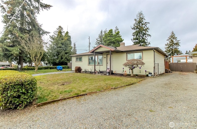 ranch-style house with a chimney, gravel driveway, fence, and a front yard