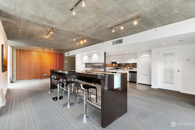 kitchen featuring carpet flooring, dishwasher, a kitchen breakfast bar, built in fridge, and white cabinets