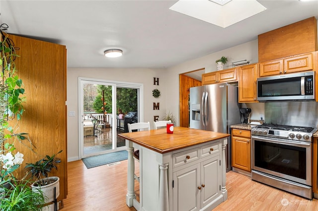 kitchen with appliances with stainless steel finishes, a center island, light hardwood / wood-style floors, and lofted ceiling with skylight