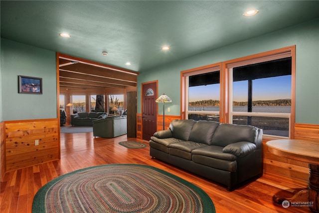 living room with wood-type flooring, a water view, and wooden walls