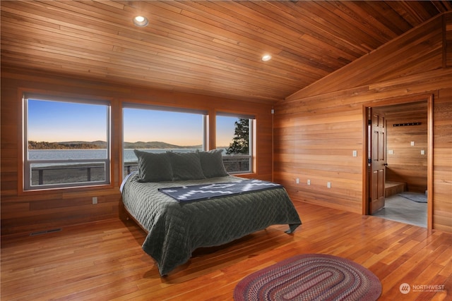 bedroom with vaulted ceiling, light wood-type flooring, and wooden walls