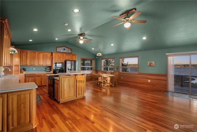 kitchen with black appliances, a center island, hardwood / wood-style floors, sink, and a water view