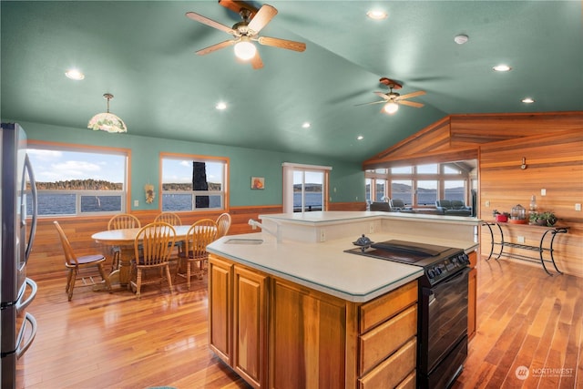 kitchen with pendant lighting, lofted ceiling, wooden walls, black range with electric cooktop, and stainless steel fridge