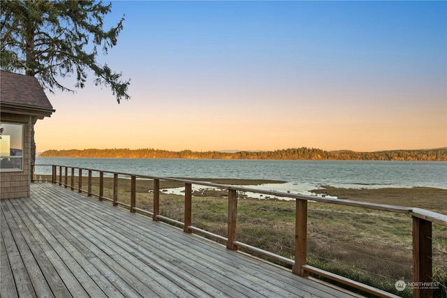 deck at dusk featuring a water view