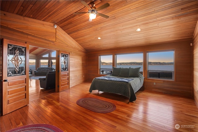 bedroom with ceiling fan, light hardwood / wood-style flooring, wood walls, and a water view