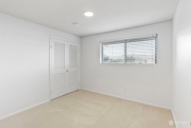 unfurnished bedroom featuring light carpet, baseboards, and a closet