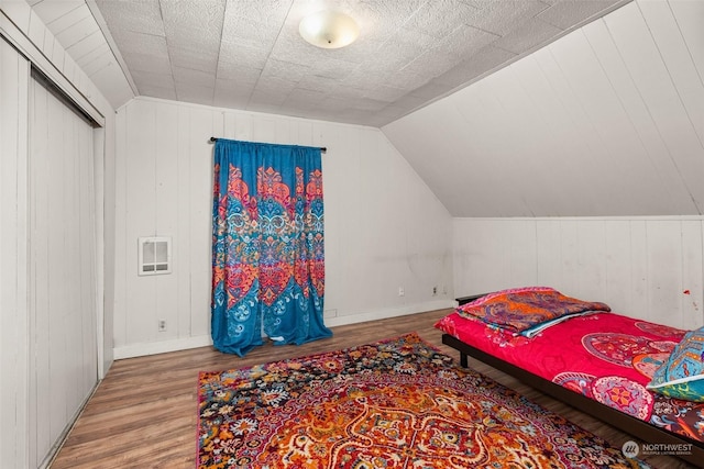 bedroom featuring wooden walls, a closet, wood-type flooring, and vaulted ceiling