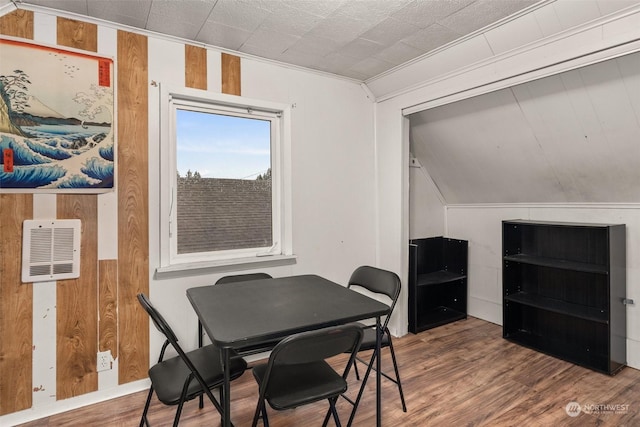 dining area featuring hardwood / wood-style flooring, wood walls, ornamental molding, and vaulted ceiling