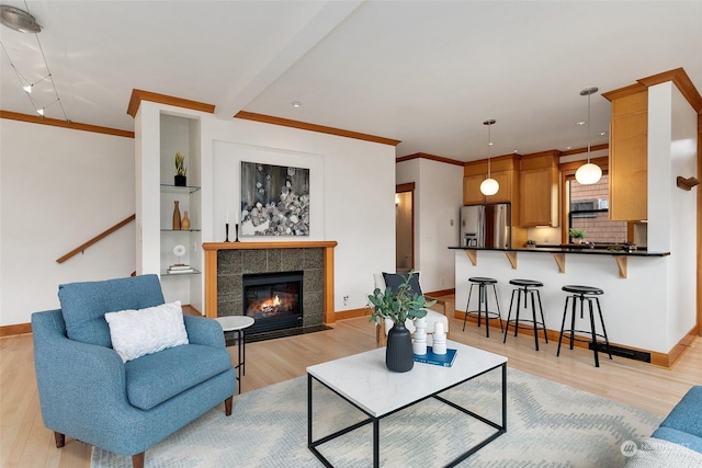 living room with a tiled fireplace, crown molding, and light hardwood / wood-style floors