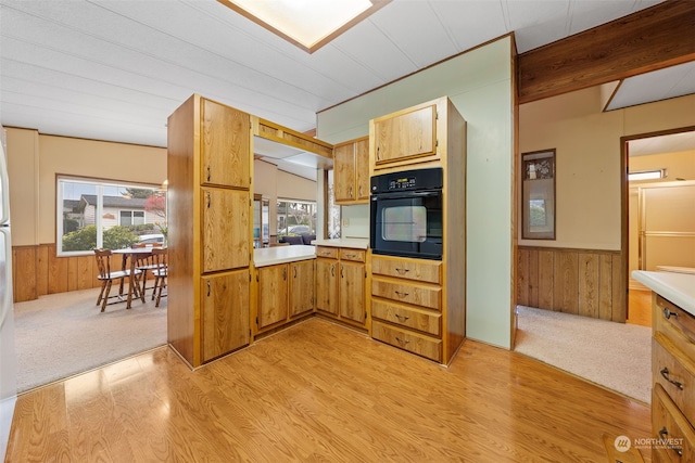 kitchen featuring wood walls, black oven, and light hardwood / wood-style flooring