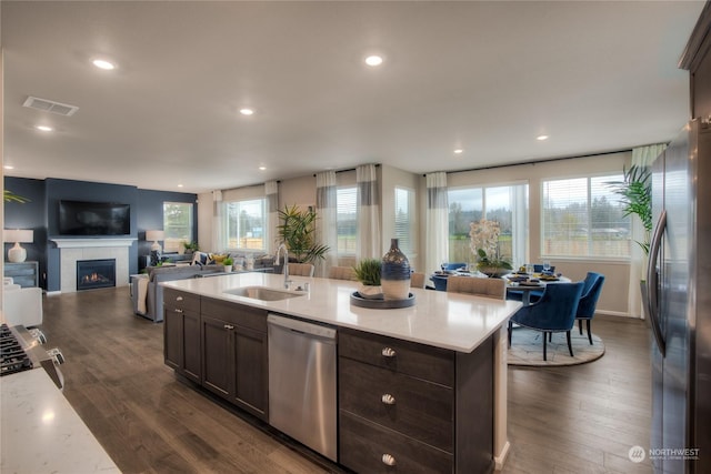 kitchen with a kitchen island with sink, sink, appliances with stainless steel finishes, and dark wood-type flooring