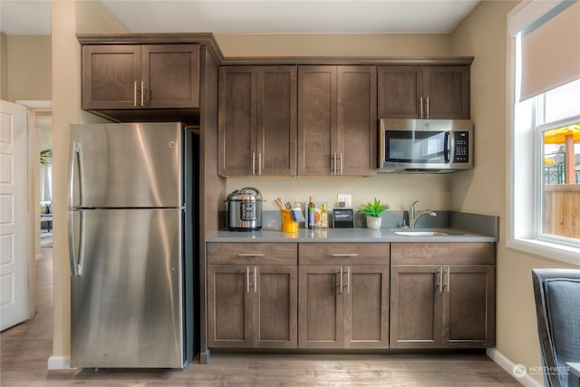 kitchen with dark brown cabinetry, sink, stainless steel appliances, and light hardwood / wood-style flooring