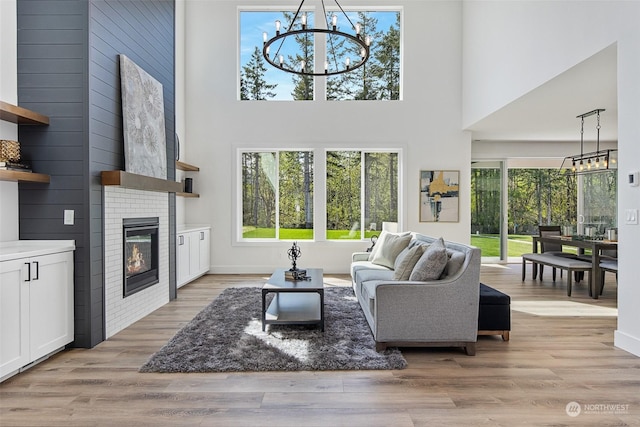 living room with an inviting chandelier, a large fireplace, light hardwood / wood-style flooring, and a towering ceiling