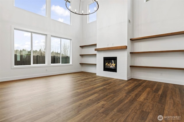 unfurnished living room featuring a chandelier, a fireplace, plenty of natural light, and wood finished floors