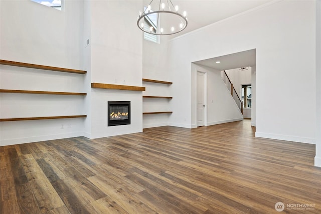 unfurnished living room featuring a notable chandelier, a fireplace, baseboards, and wood finished floors