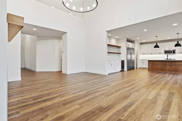 unfurnished living room with wine cooler, a notable chandelier, recessed lighting, light wood-style floors, and baseboards