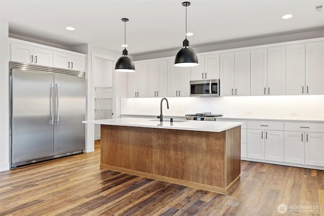 kitchen featuring stainless steel appliances, white cabinetry, a sink, and wood finished floors