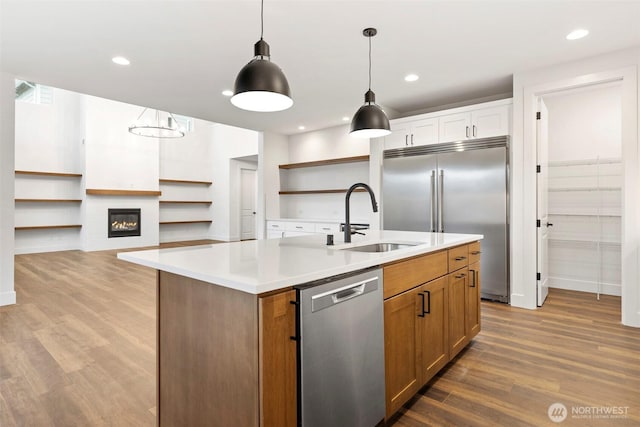 kitchen with appliances with stainless steel finishes, wood finished floors, light countertops, open shelves, and a sink